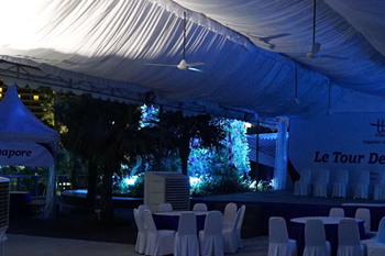 A-shaped tent at night with blue ambient lighting, white chairs, event branding banner, no people