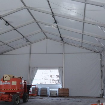 interior of large empty white aluminium tent structure, exposed truss ceiling, orange scissor lifts inside, construction setup phase