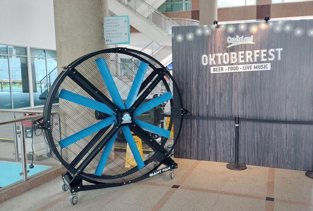 large industrial standing fan in mall lobby near Oktoberfest event signage backdrop with string lights