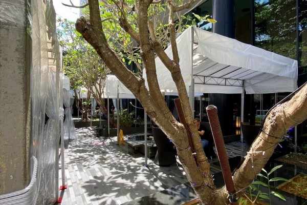 small white pop-up canopy tent set up in narrow urban courtyard walkway, trees and buildings surrounding, tight space