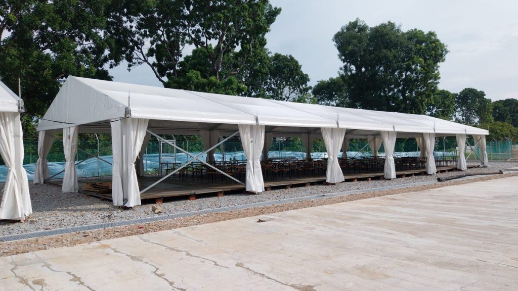 outdoor white marquee tent with draped side curtains on gravel ground, trees in background, empty, cloudy daytime