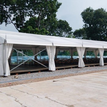 outdoor white marquee tent with draped side curtains on gravel ground, trees in background, empty, cloudy daytime