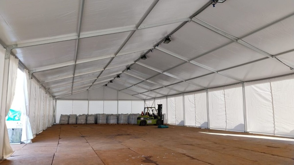interior of white industrial storage tent, forklift and stacked pallets on one side, wooden floor covering