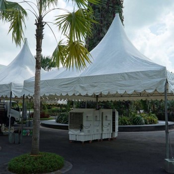 white pagoda tent set up in landscaped garden roundabout with palm trees, portable aircon units on ground, resort setting