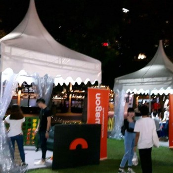 white pagoda tents with clear PVC sides at night lifestyle event, branded orange booth, people mingling
