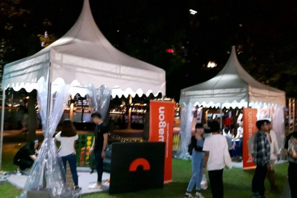 white pagoda tents with clear PVC sides at night lifestyle event, branded orange booth, people mingling