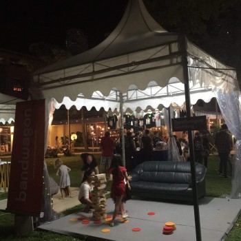 white pagoda tent at night garden festival event, people playing lawn game, sofa nearby, festive evening event