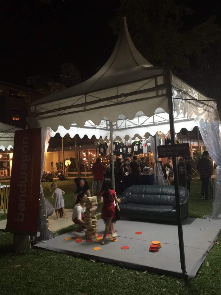 white pagoda tent at night garden festival event, people playing lawn game, sofa nearby, festive evening event