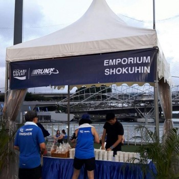 white pagoda tent with branded sports run event banner, waterfront setting, runners at finish line