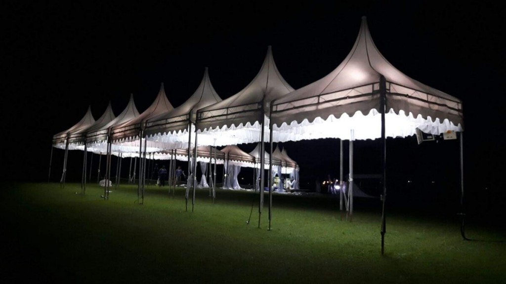 row of white pagoda tents lit up at night on grass field, empty, dark night sky