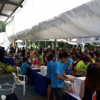 outdoor community bazaar under white tent canopy, crowd of people browsing $20 pricing sale tables, HDB void deck setting, daytime