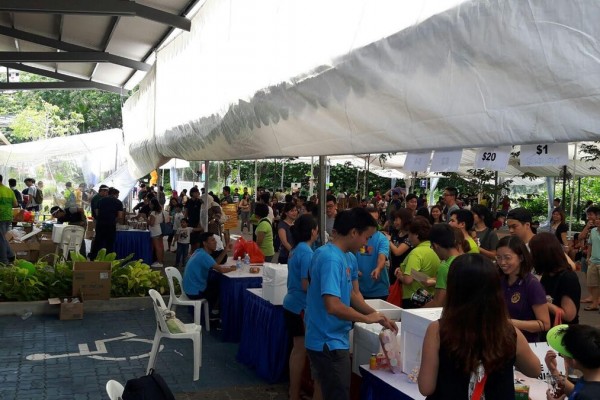 outdoor community bazaar under white tent canopy, crowd of people browsing $20 pricing sale tables, HDB void deck setting, daytime