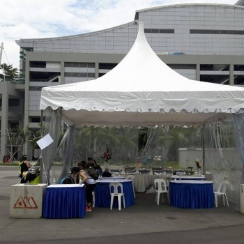 white pagoda tent outdoor booth with blue-skirted tables, city building backdrop, staff and visitors present