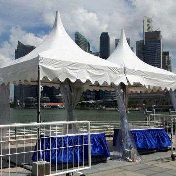 two white pagoda tents on waterfront promenade, Singapore skyline in background, blue-clothed booth setup, barrier fencing