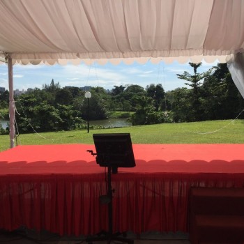 white draped tent overlooking scenic green garden view with pond, red-skirted table and lectern setup, curtain drawn back