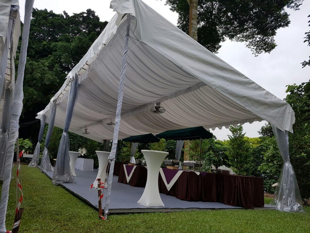 white draped tent with hanging fabric drapes, small cocktail table with dark tablecloth, outdoor garden setting, empty before event