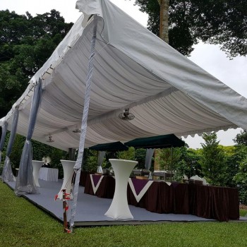 white draped tent with hanging fabric drapes, small cocktail table with dark tablecloth, outdoor garden setting, empty before event