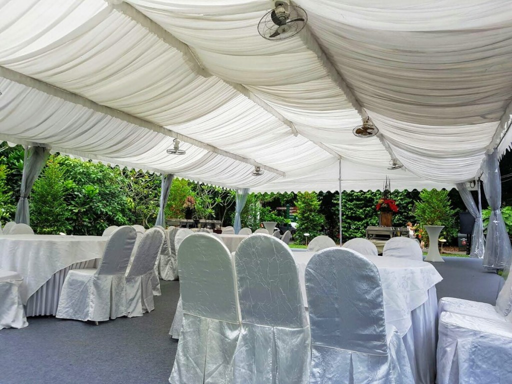 white draped tent ceiling with standing fan, rows of satin white chair covers, outdoor garden setting, empty before event
