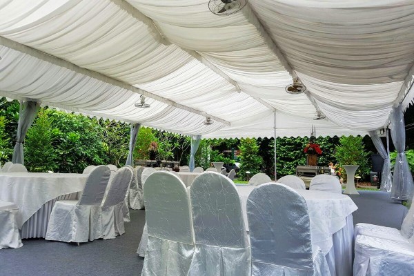 white draped tent ceiling with standing fan, rows of satin white chair covers, outdoor garden setting, empty before event
