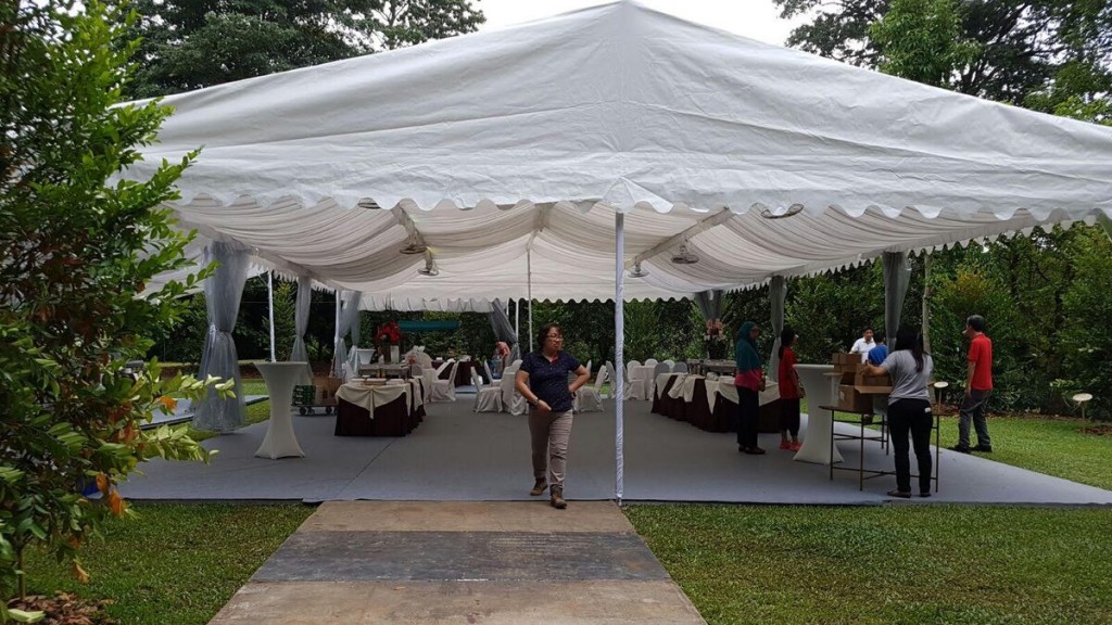 white square-top canopy tent in garden, staff setting up round tables with tablecloths underneath, daytime