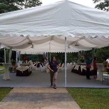 white square-top canopy tent in garden, staff setting up round tables with tablecloths underneath, daytime