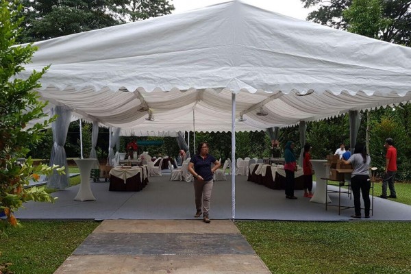 white square-top canopy tent in garden, staff setting up round tables with tablecloths underneath, daytime