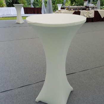 outdoor wedding reception, white cocktail table under draped white tent, buffet tables and floral centerpiece in background, garden setting