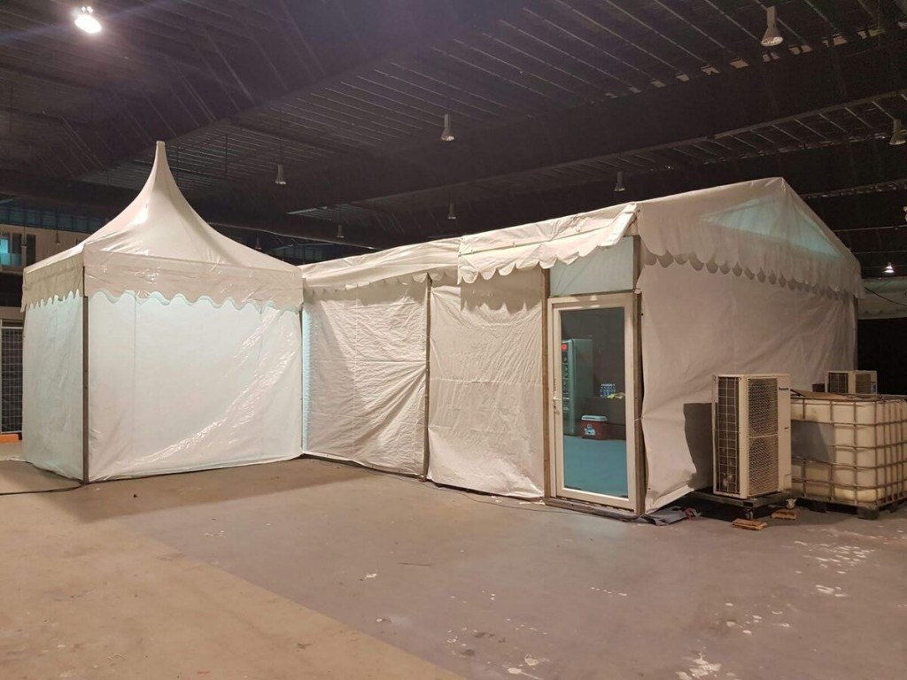 white peaked pagoda tent set up indoors in warehouse, water tank containers stacked nearby, empty