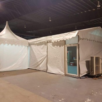white peaked pagoda tent set up indoors in warehouse, water tank containers stacked nearby, empty