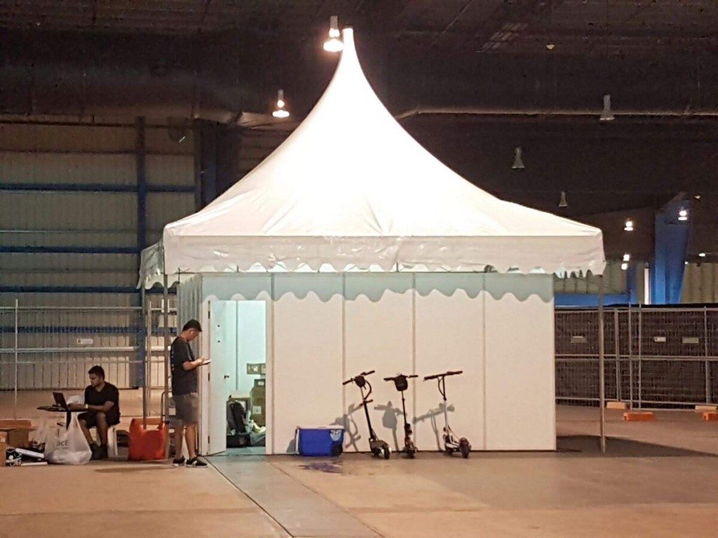 white peaked pagoda tent set up indoors in warehouse, person standing near entrance, e-scooters parked outside