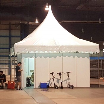 white peaked pagoda tent set up indoors in warehouse, person standing near entrance, e-scooters parked outside