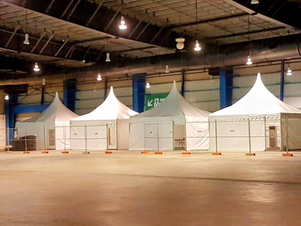 indoor warehouse storage with several white peaked pop-up canopy tents set up in a row, concrete floor, no people