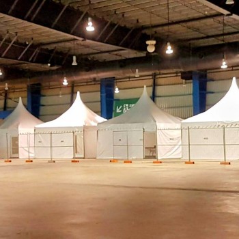 indoor warehouse storage with several white peaked pop-up canopy tents set up in a row, concrete floor, no people