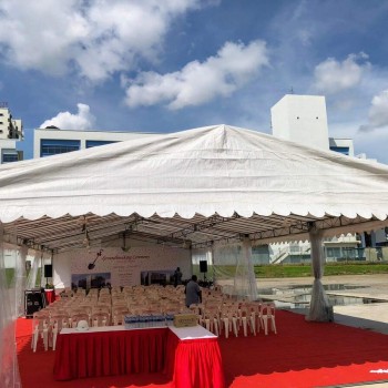 white tent with red carpet flooring, gold chairs set up for corporate event, industrial building in background, empty before guests