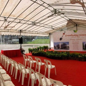 white tent with clear PVC roof panels, red carpet aisle with white chairs set up for corporate groundbreaking ceremony, stage with podium