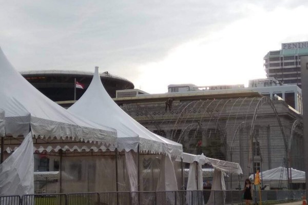 white A-frame tent along building with domed roof, barrier fencing, person standing, overcast daytime