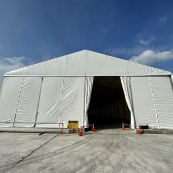 outdoor daytime white A-frame tent exterior, open entrance, traffic cones, car park area in background, empty, no people
