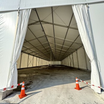 interior view of empty white event tent looking down center aisle, traffic cones at entrance, daytime, no people
