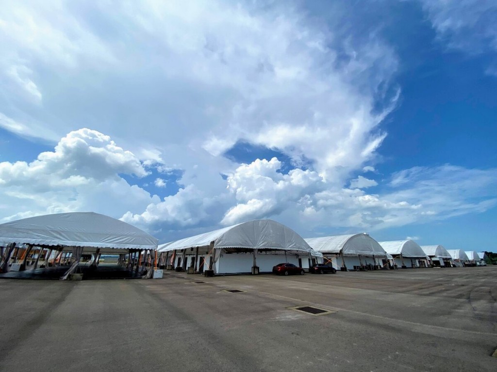 outdoor row of dome-shaped tents seen from a distance, empty lot, dramatic cloudy sky, daytime, no people