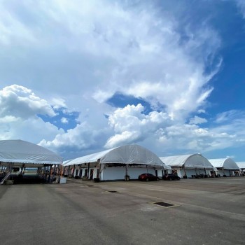 outdoor row of dome-shaped tents seen from a distance, empty lot, dramatic cloudy sky, daytime, no people