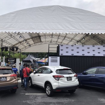 white canopy tent at outdoor car park event with LED screen backdrop, cars parked nearby, people gathered, daytime
