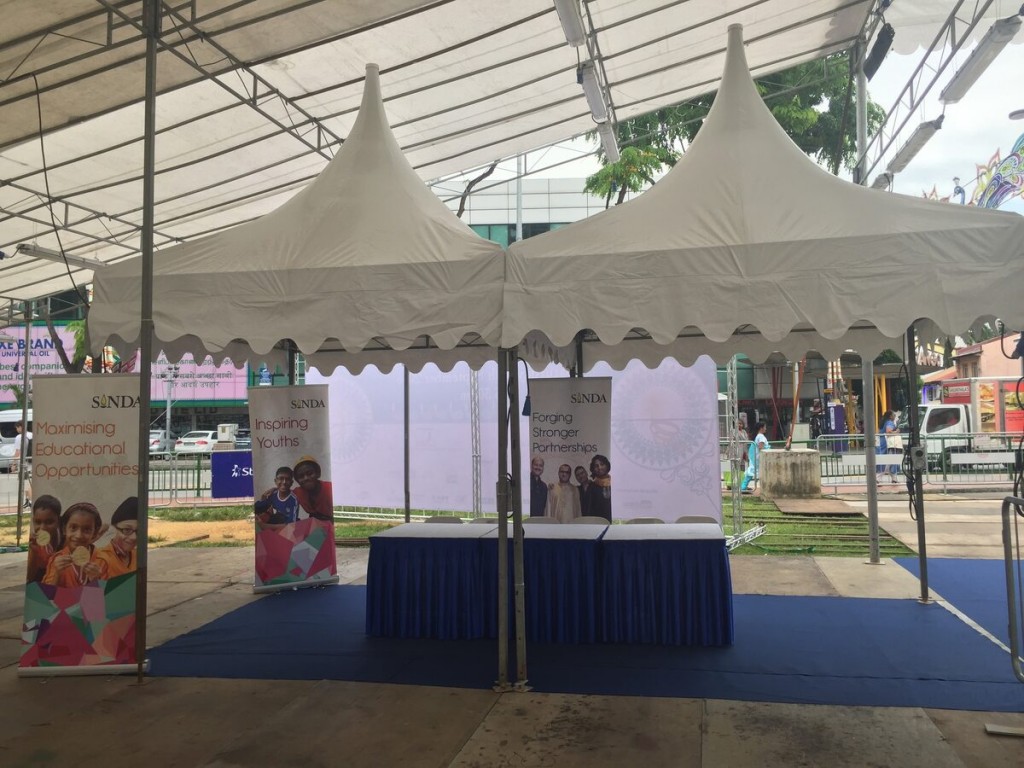 beige pagoda tents at outdoor street community outreach event, blue-skirted table with informational banner stands