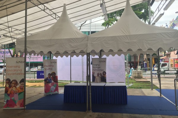 beige pagoda tents at outdoor street community outreach event, blue-skirted table with informational banner stands