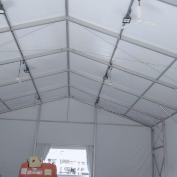 interior of empty white tent structure, exposed truss ceiling, orange scissor lift equipment at bottom, sunlit opening