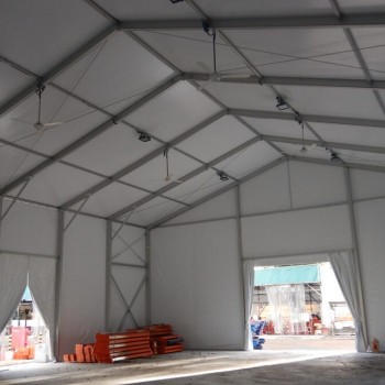 interior of empty white tent, exposed truss ceiling, storage shelving racks visible through opening, concrete floor, industrial setting