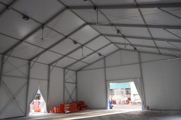 interior of empty white tent, exposed truss ceiling, storage shelving racks visible through opening, concrete floor, industrial setting