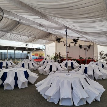 draped white tent ceiling with standing fans, round tables in white and navy skirting, white chair covers, empty tent before event