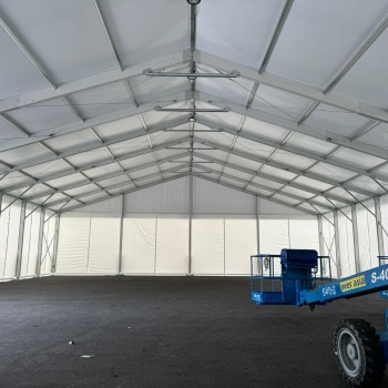 interior of empty aluminium-frame tent structure, exposed truss ceiling, scissor lift parked inside, concrete floor, under setup, no walls