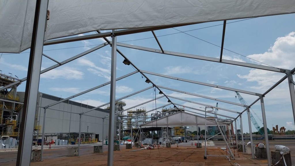 view from inside partially built tent frame roof structure looking out at industrial plant with crane, exposed aluminium trusses