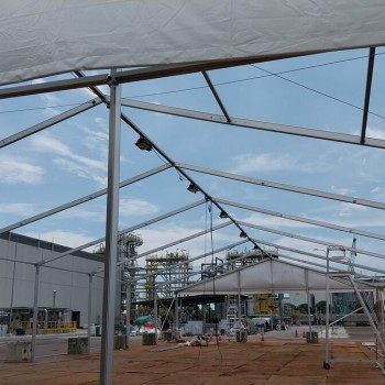 view from inside partially built tent frame roof structure looking out at industrial plant with crane, exposed aluminium trusses